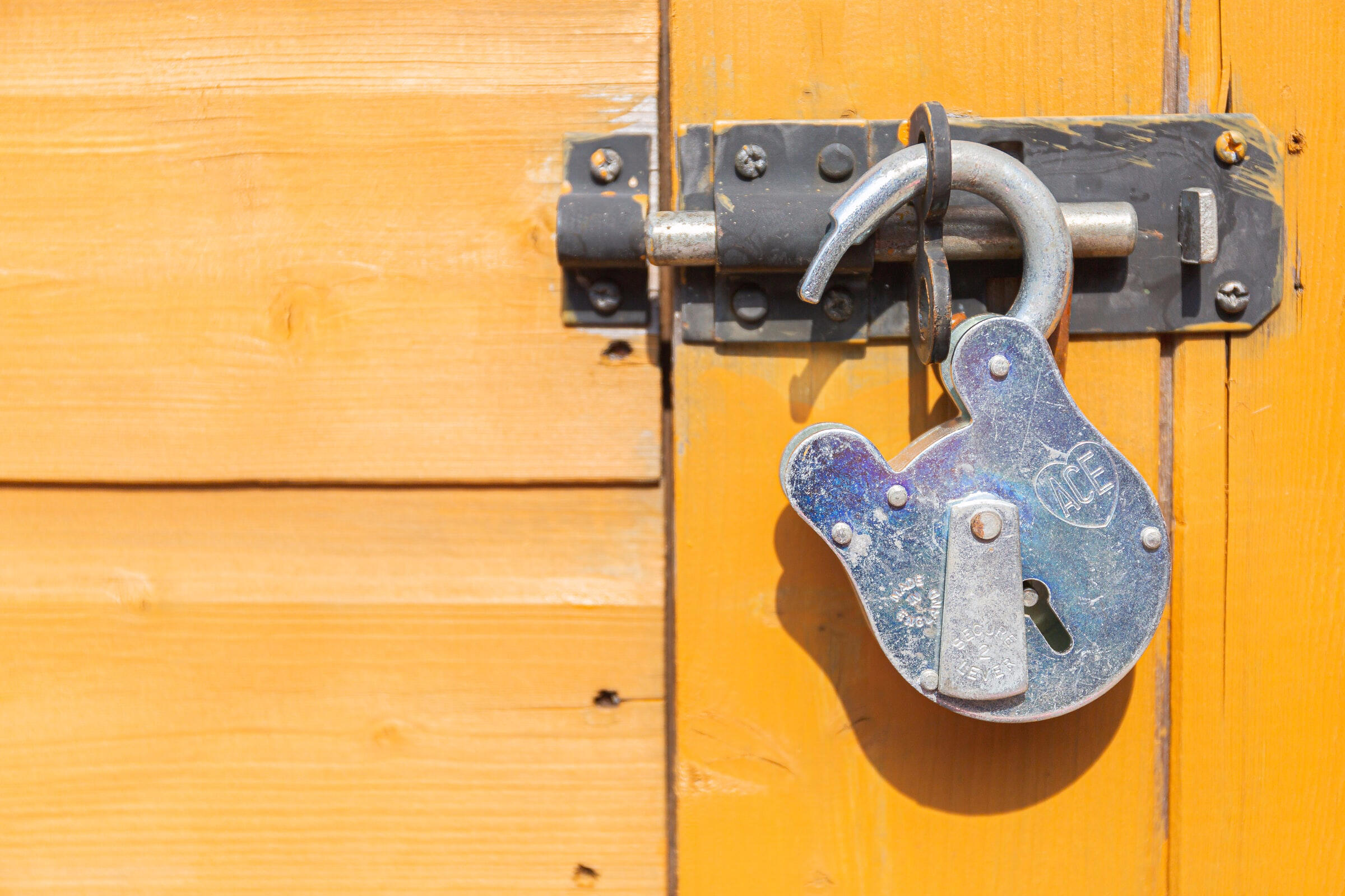 open padlock in a metal bolt on a yellow wooden door